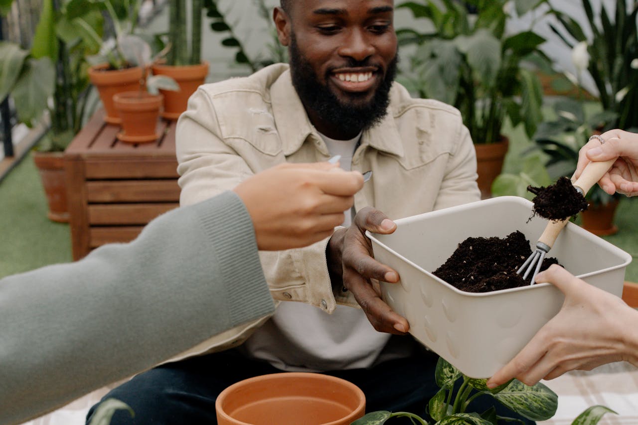 A joyful man shares a gardening moment with friends, tending to plants indoors.